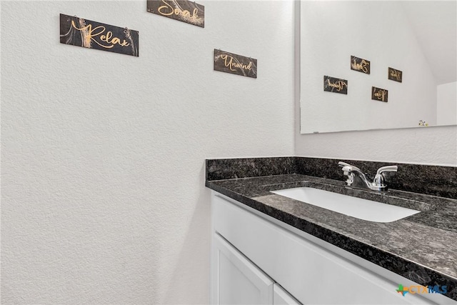 bathroom featuring a textured wall, vanity, and vaulted ceiling