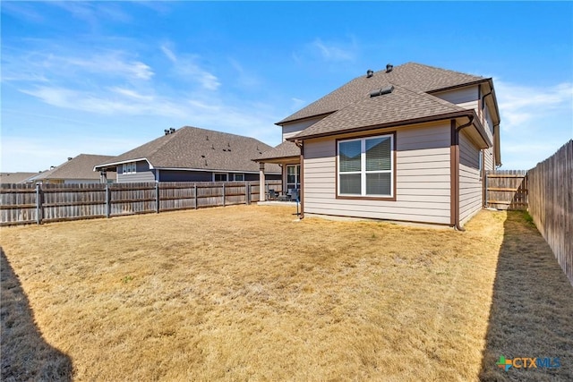 rear view of house featuring a lawn, roof with shingles, and a fenced backyard