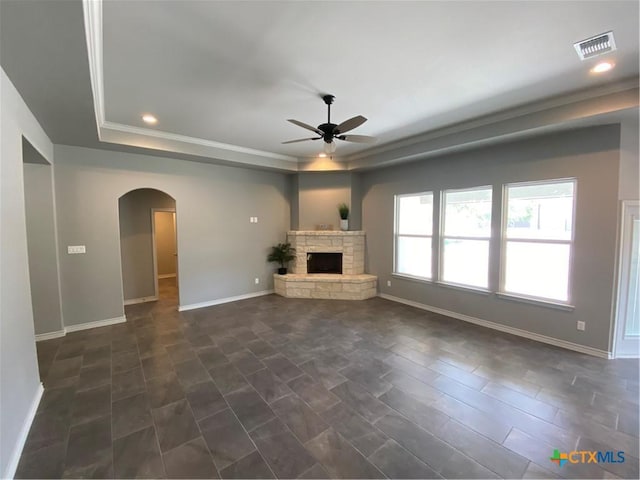 unfurnished living room featuring arched walkways, a tray ceiling, a fireplace, and visible vents