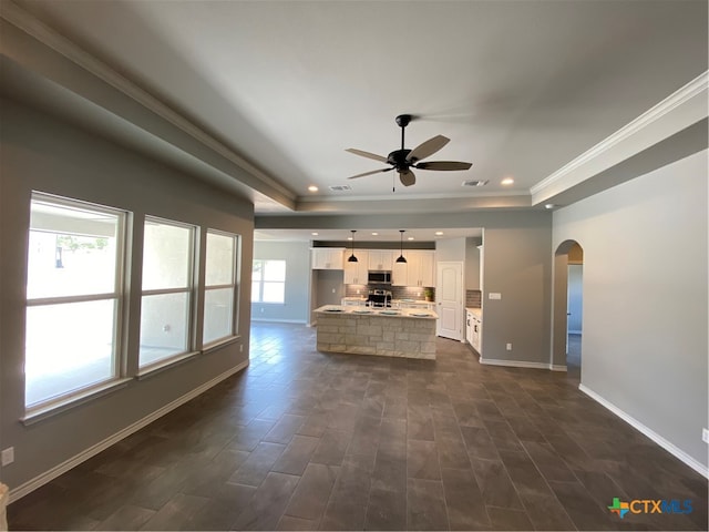 unfurnished living room featuring arched walkways, a raised ceiling, baseboards, and recessed lighting