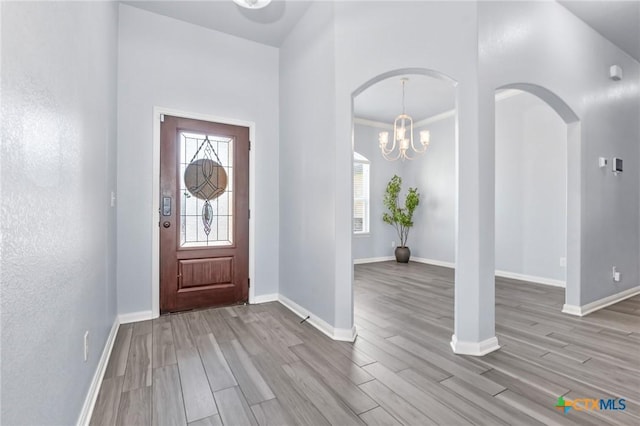 entryway with light hardwood / wood-style floors, crown molding, and an inviting chandelier