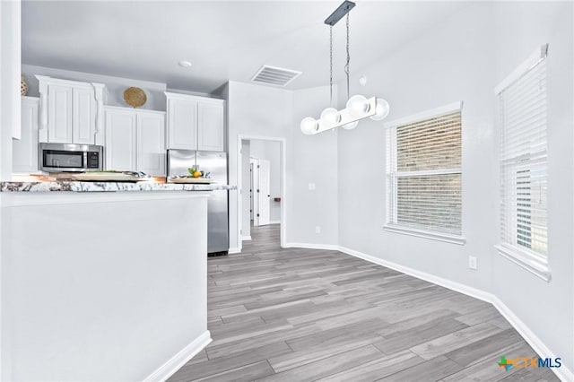 kitchen with white cabinets, decorative light fixtures, light hardwood / wood-style floors, and appliances with stainless steel finishes