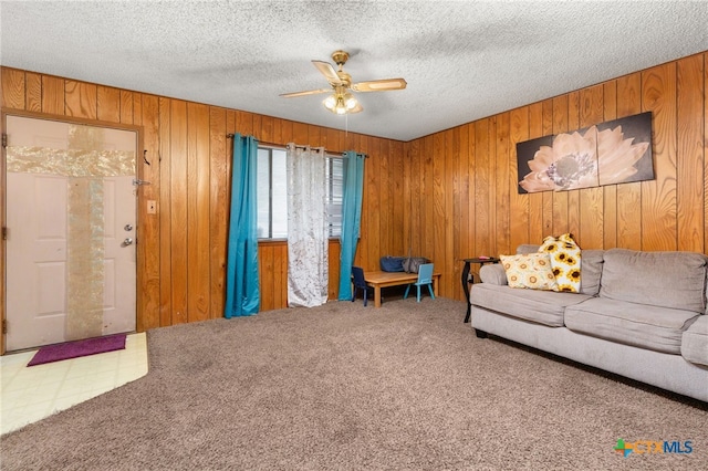 living room featuring carpet, ceiling fan, wood walls, and a textured ceiling