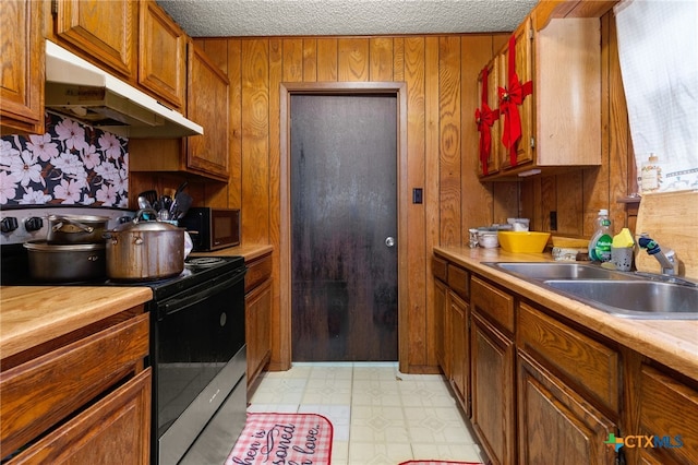 kitchen with a textured ceiling, stainless steel electric range oven, sink, and wood walls