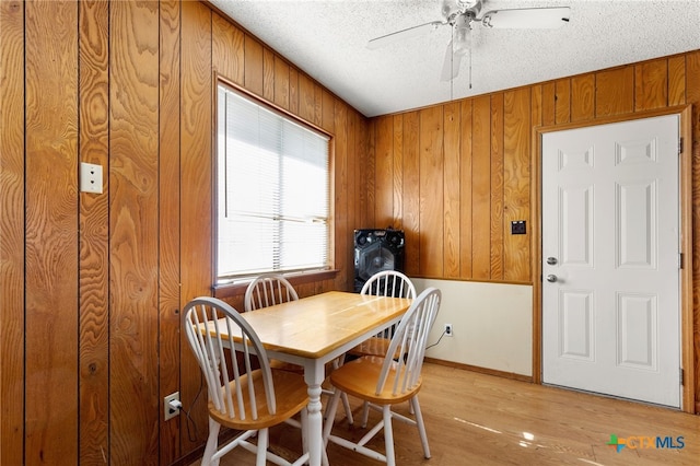 dining area featuring a textured ceiling, light wood-type flooring, ceiling fan, and wooden walls