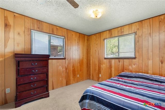 carpeted bedroom with wooden walls, ceiling fan, and a textured ceiling