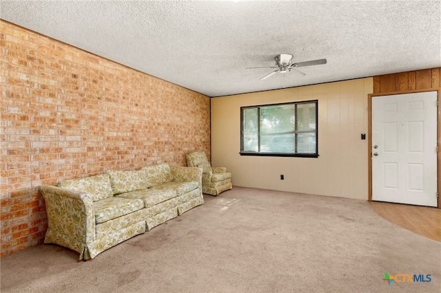 unfurnished living room with ceiling fan, brick wall, a textured ceiling, wooden walls, and carpet