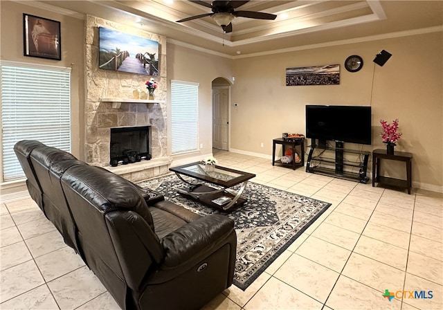 tiled living room featuring ceiling fan, a raised ceiling, ornamental molding, and a fireplace