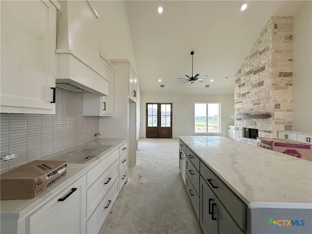 kitchen featuring tasteful backsplash, a ceiling fan, white cabinetry, custom range hood, and cooktop