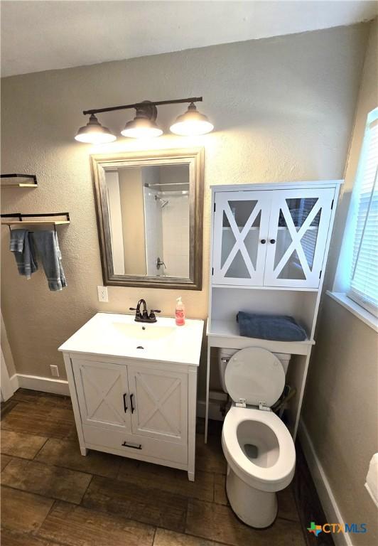 bathroom with a textured wall, baseboards, vanity, and toilet