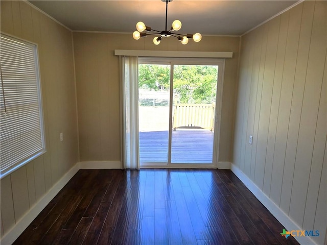 unfurnished room featuring baseboards, an inviting chandelier, dark wood-type flooring, and ornamental molding