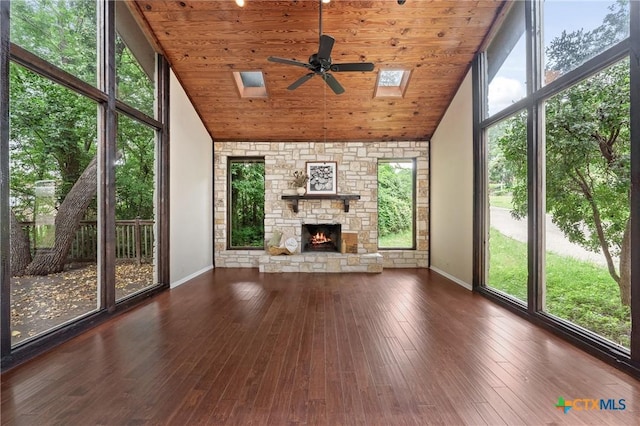 unfurnished sunroom with a stone fireplace, ceiling fan, vaulted ceiling with skylight, and wooden ceiling