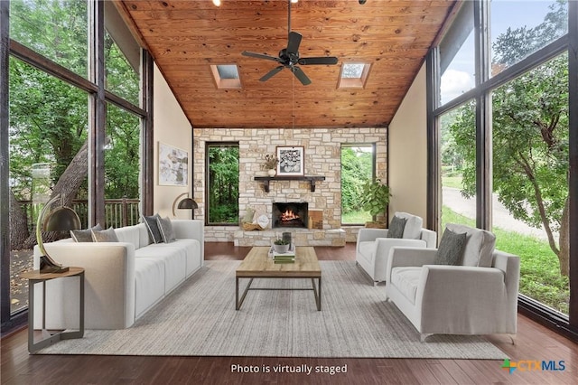 sunroom / solarium featuring a fireplace, ceiling fan, vaulted ceiling with skylight, and wooden ceiling