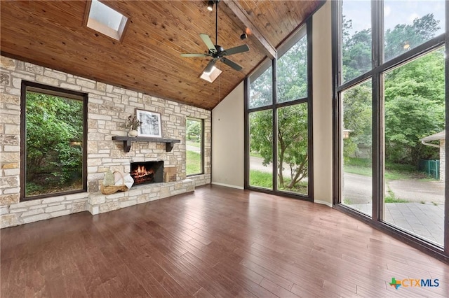 unfurnished living room with hardwood / wood-style floors, high vaulted ceiling, a stone fireplace, a skylight, and ceiling fan