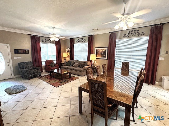 tiled dining room with ceiling fan, ornamental molding, and a textured ceiling