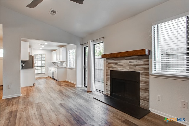 unfurnished living room featuring light wood-type flooring, a tiled fireplace, lofted ceiling, and a healthy amount of sunlight