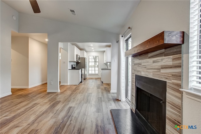 unfurnished living room with light hardwood / wood-style floors, ceiling fan, a tile fireplace, and vaulted ceiling