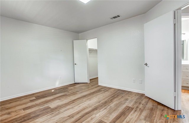 unfurnished bedroom with connected bathroom, a closet, light wood-type flooring, and a walk in closet