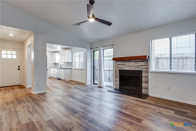 unfurnished living room with sink, ceiling fan, light hardwood / wood-style flooring, a tile fireplace, and vaulted ceiling