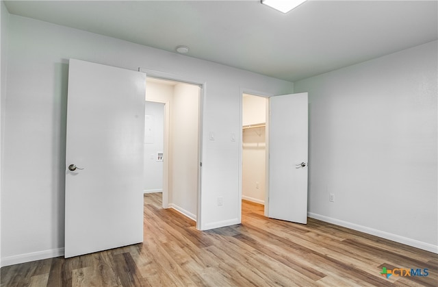 unfurnished bedroom with light hardwood / wood-style flooring, a spacious closet, and a closet