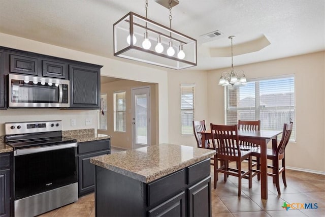 kitchen with visible vents, appliances with stainless steel finishes, a center island, a tray ceiling, and an inviting chandelier