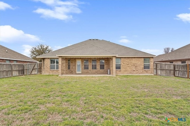 rear view of property with brick siding, a patio, a fenced backyard, and a lawn