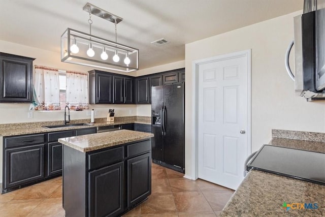 kitchen featuring visible vents, stainless steel microwave, dark cabinets, black fridge, and a sink