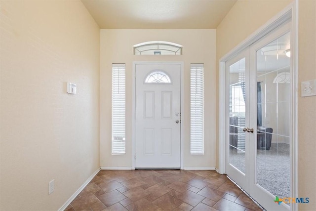 foyer entrance with a healthy amount of sunlight, stone finish flooring, baseboards, and french doors