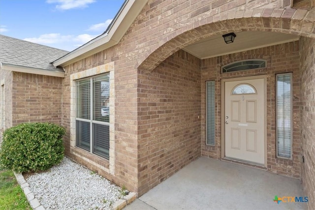 property entrance with a shingled roof and brick siding