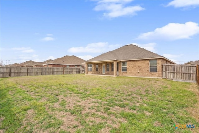 back of house with a yard, brick siding, a patio area, and a fenced backyard