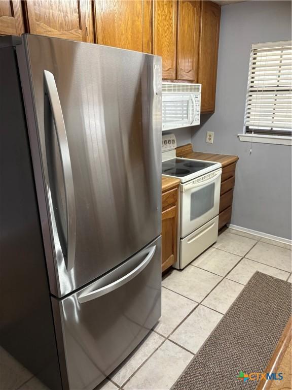 kitchen featuring light countertops, white appliances, brown cabinetry, and light tile patterned flooring