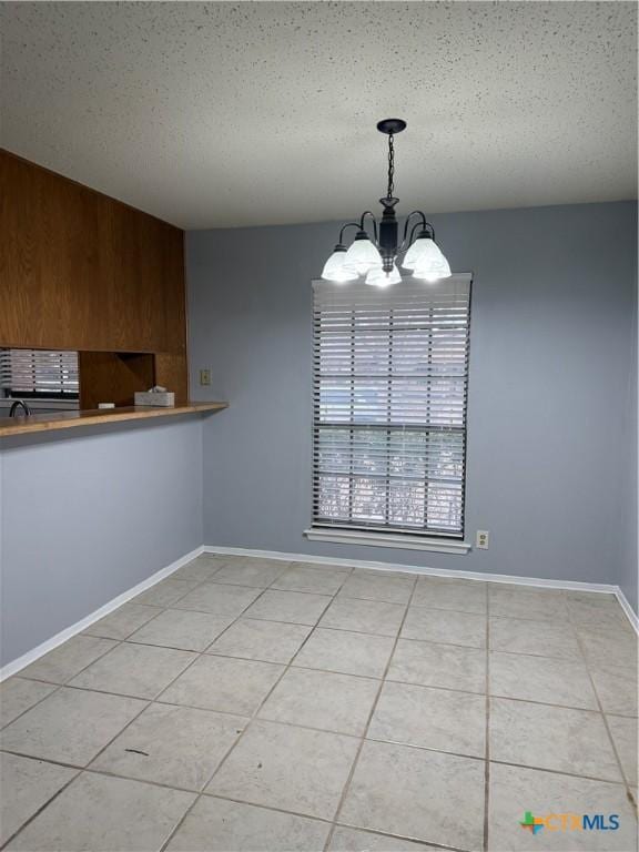 unfurnished dining area featuring light tile patterned floors, baseboards, a chandelier, and a textured ceiling