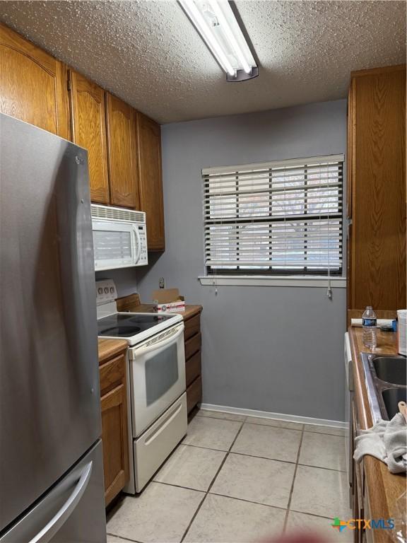 kitchen featuring light tile patterned floors, a textured ceiling, and white appliances