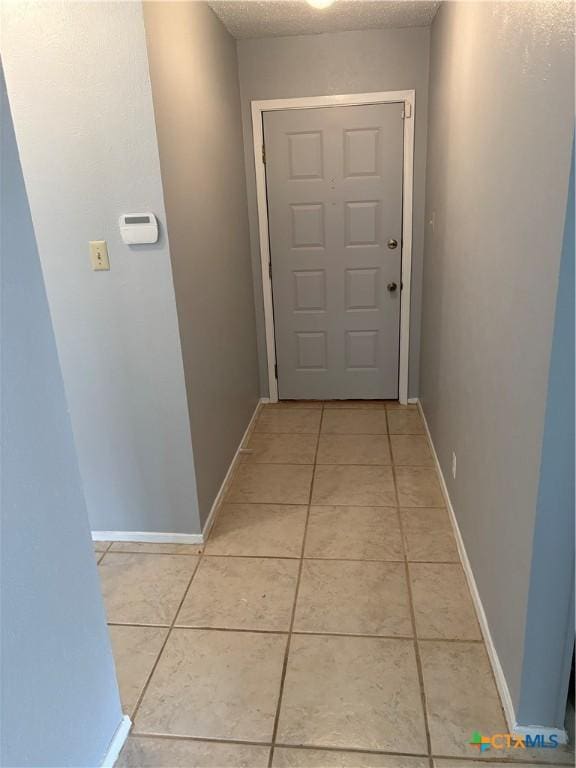 hallway featuring baseboards, a textured ceiling, and light tile patterned flooring