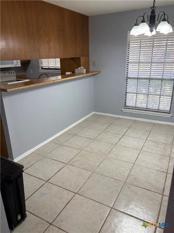 kitchen with white microwave, tile patterned flooring, electric range, hanging light fixtures, and an inviting chandelier