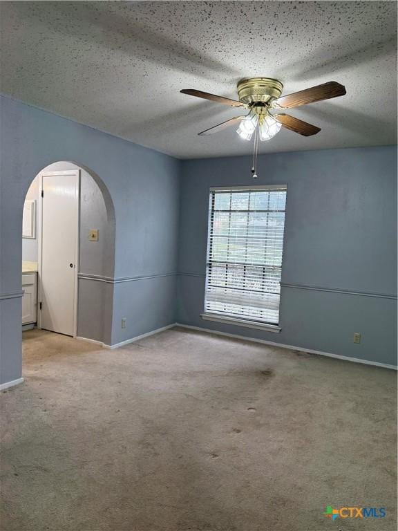 empty room featuring arched walkways, a textured ceiling, baseboards, and light colored carpet