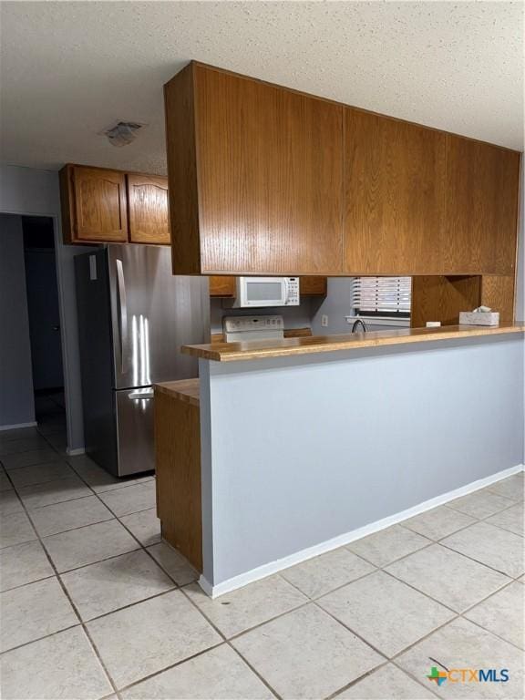 kitchen featuring white microwave, brown cabinets, freestanding refrigerator, a peninsula, and light countertops