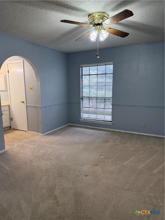 carpeted spare room with arched walkways, ceiling fan, a textured ceiling, and baseboards