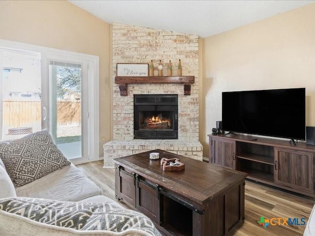 living room with lofted ceiling, a brick fireplace, and light wood-type flooring