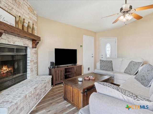 living room featuring hardwood / wood-style flooring, ceiling fan, lofted ceiling, and a brick fireplace