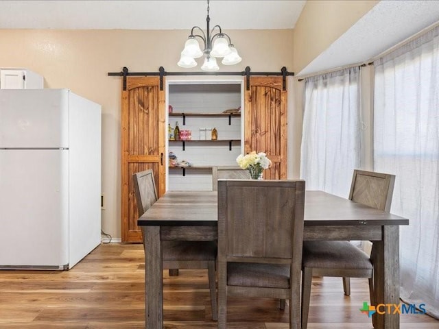 dining area with a barn door, a notable chandelier, and light hardwood / wood-style flooring