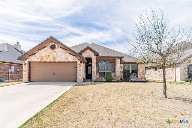 french country style house featuring brick siding, concrete driveway, a front yard, a garage, and stone siding