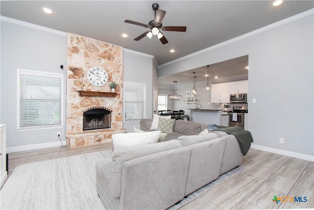 living room featuring wood finish floors, a ceiling fan, a stone fireplace, crown molding, and baseboards