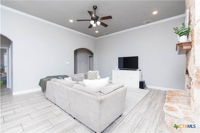 living area featuring visible vents, a ceiling fan, arched walkways, crown molding, and baseboards