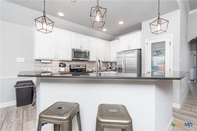 kitchen with backsplash, dark countertops, white cabinetry, appliances with stainless steel finishes, and a breakfast bar area