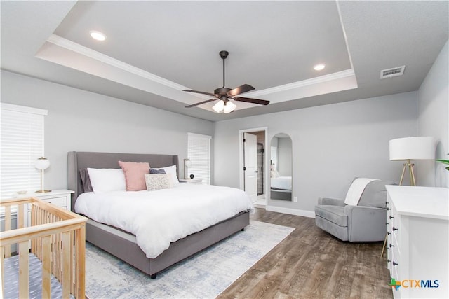 bedroom featuring a raised ceiling, crown molding, wood finished floors, and visible vents