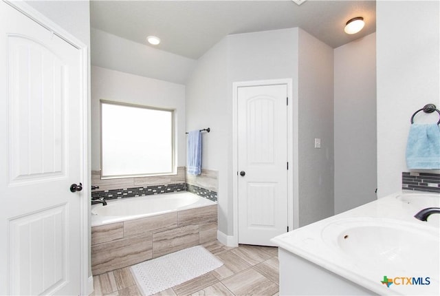 bathroom with double vanity, vaulted ceiling, a garden tub, and a sink