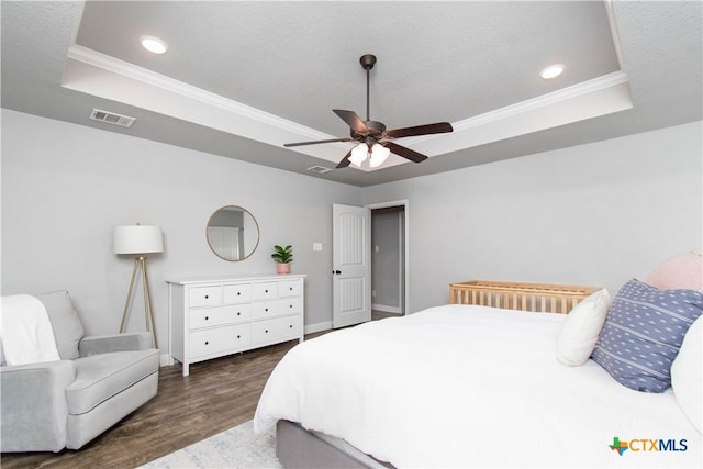 bedroom featuring a raised ceiling, crown molding, wood finished floors, and visible vents