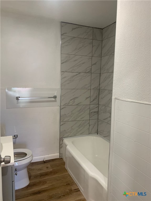 full bathroom with toilet, tile walls, tiled shower / bath, hardwood / wood-style flooring, and vanity