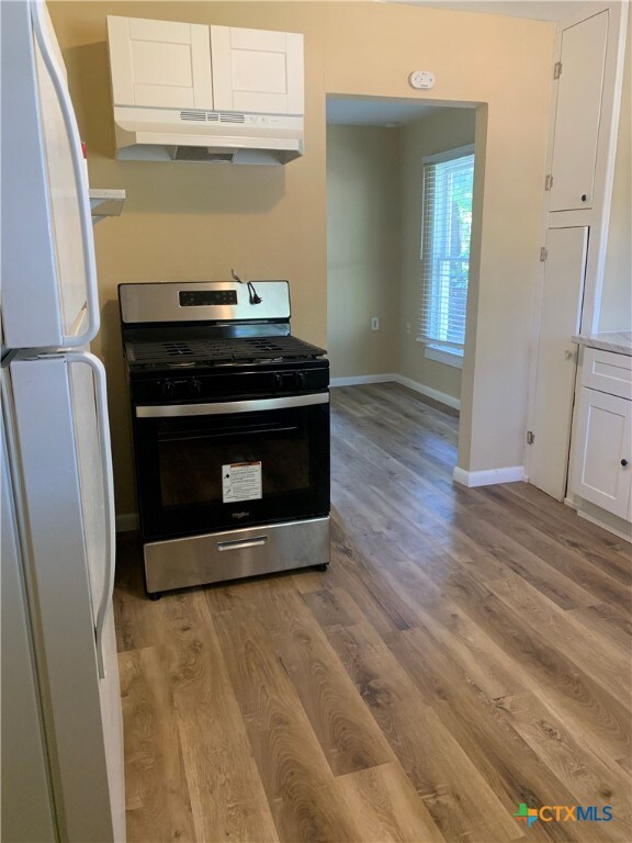 kitchen with white refrigerator, white cabinetry, stainless steel range with gas cooktop, and light hardwood / wood-style floors